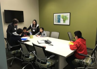 Students sit around a table engaging in a measuring activity